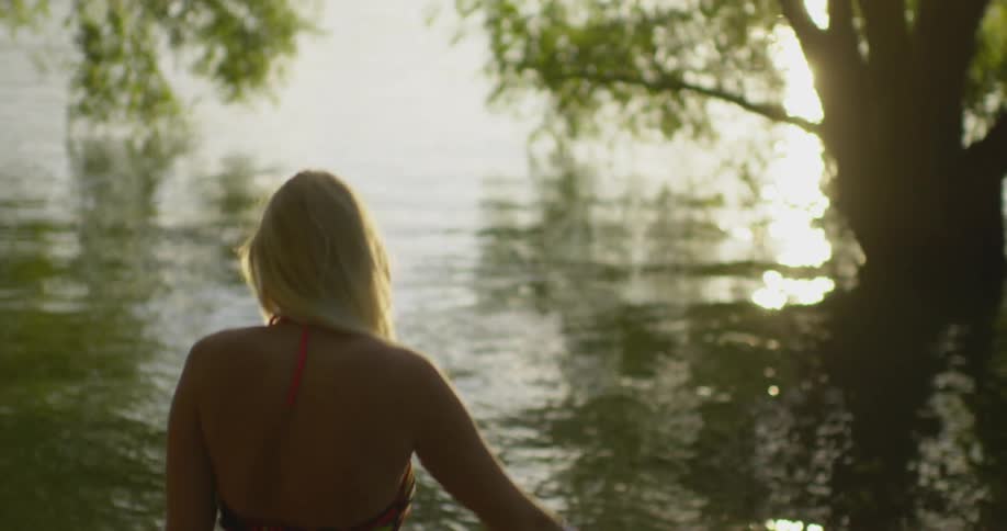 A woman takes off her t shirt as she walks toward the lake