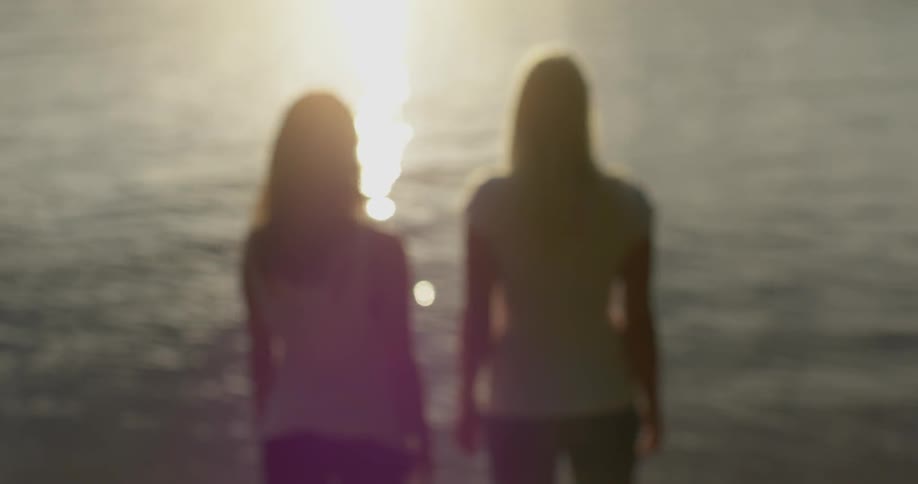 Two girls stand next to a lake at sunset