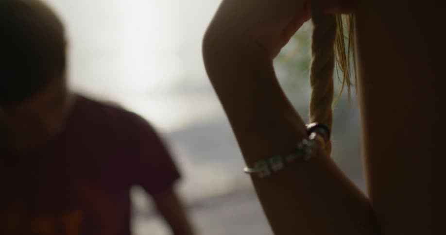 A woman sits on a rope swing next to a lake at sunset