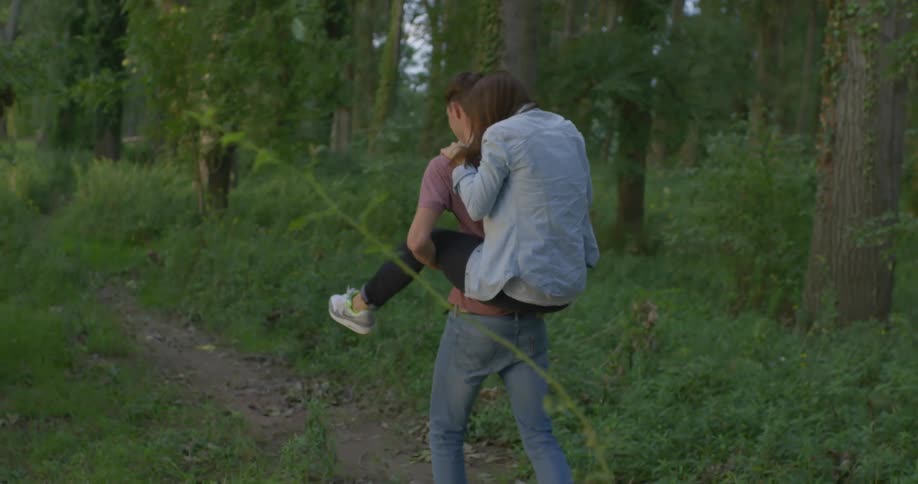 A woman piggybacks on a man walking on a trail