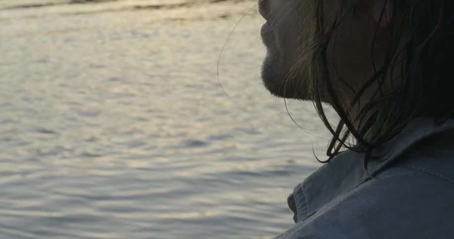 A man stands by the water at sunset