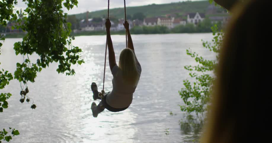 Woman plays on a rope swing next to a lake
