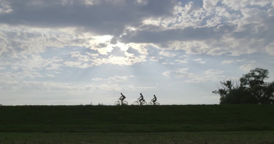 Silhouettes of people ride bicycles on a grassy ridge