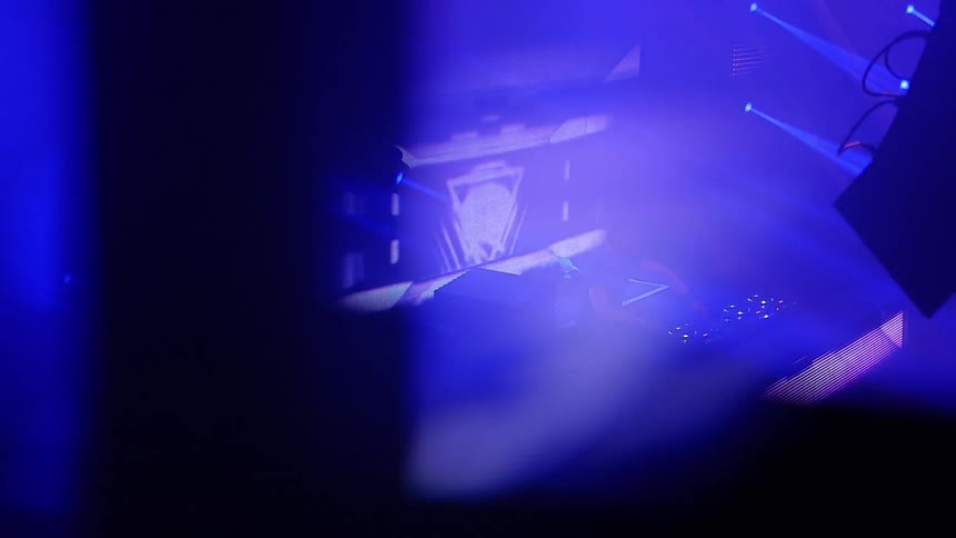 A dj is performing on a stage illuminated by flashing lights