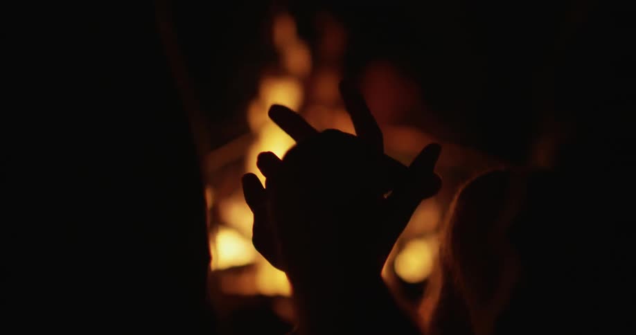Two people hold hands next to a campfire at night