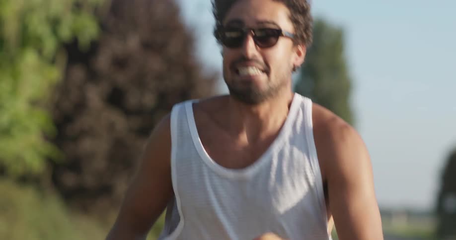 A man in a tank top and sunglasses runs on a sunny day