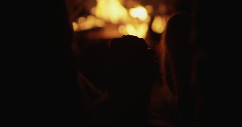 Two people hold hands next to a campfire at night