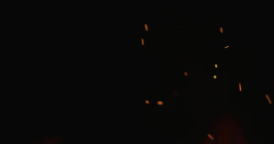 Embers from a campfire fly through the night air