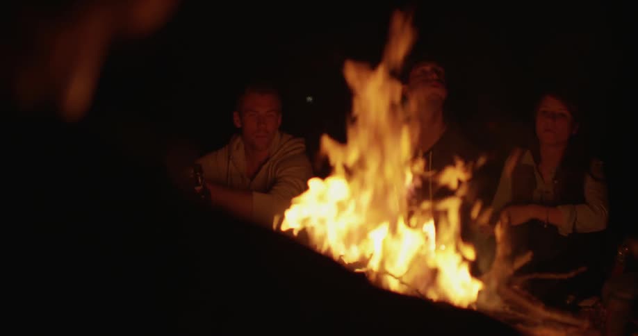 Friends surround a campfire at night