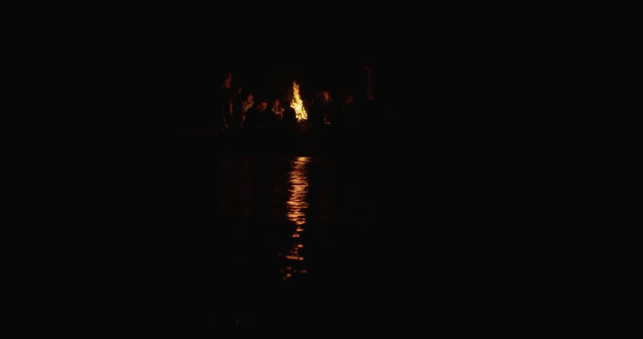 People sitting around a bonfire near a lake