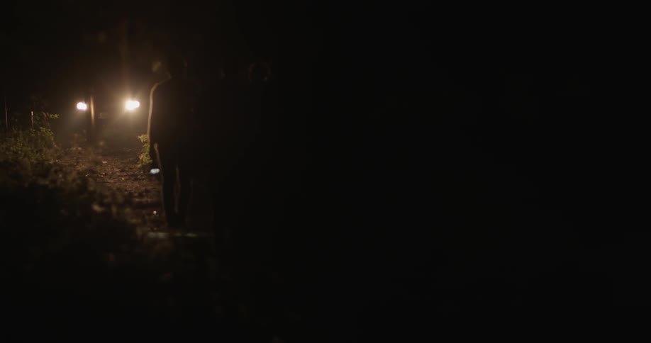 Two people are walking on a dirt path at night