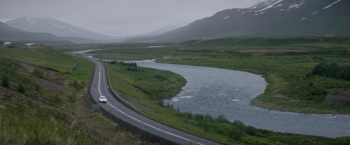 A car is driving on a road past a river in a mountain landscape during the day