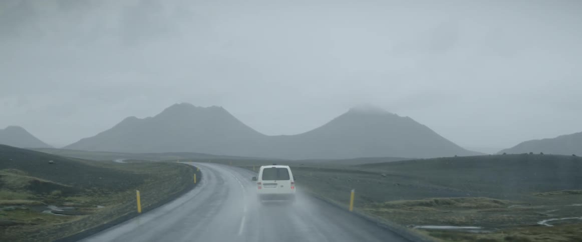 Cars drive on a rural mountain road during a rainstorm