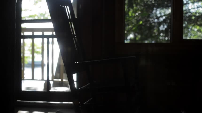 A man sets a rocking chair rocking as he walks through a room during the day
