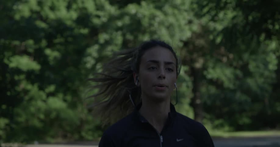 A woman is jogging outside by the trees