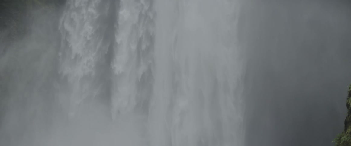 A waterfall is cascading into a pool at the bottom of cliffs during the day