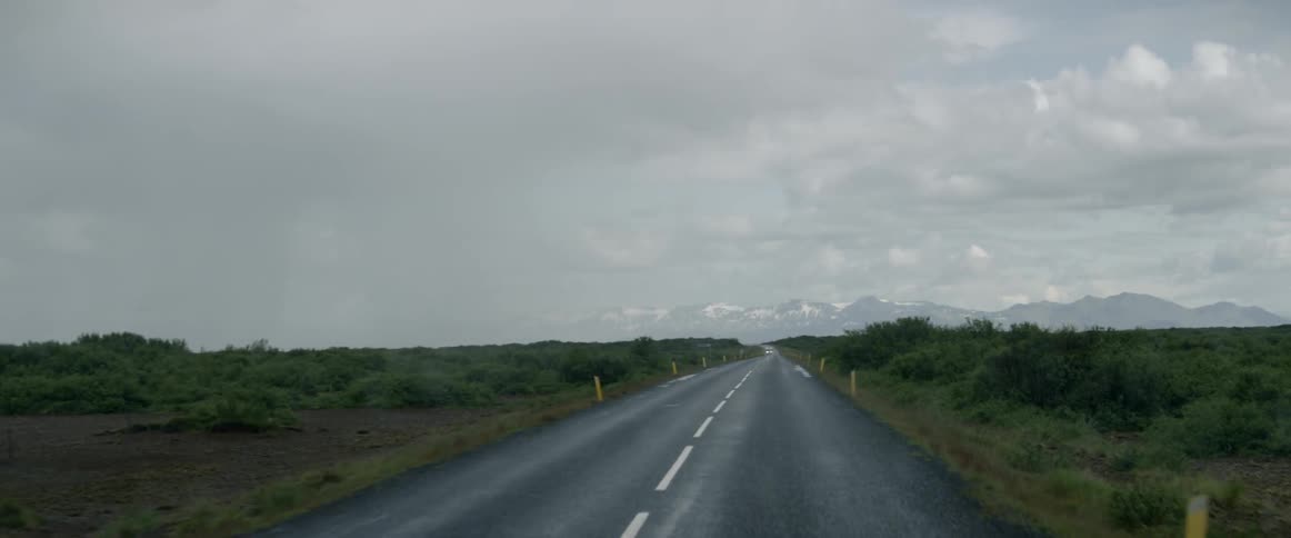 A vehicle drives on a rural road on a rainy day