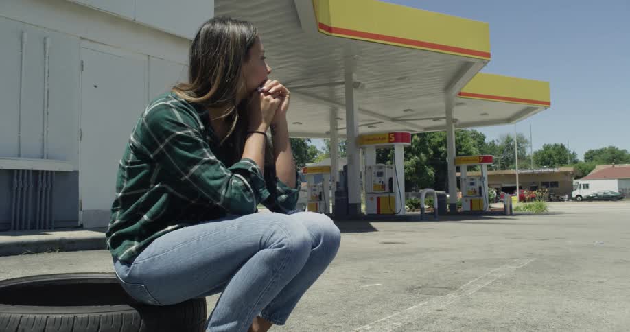 A woman sits on a tire in a gas station parking lot