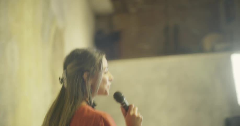 A woman in an orange microphone walks out on to stage