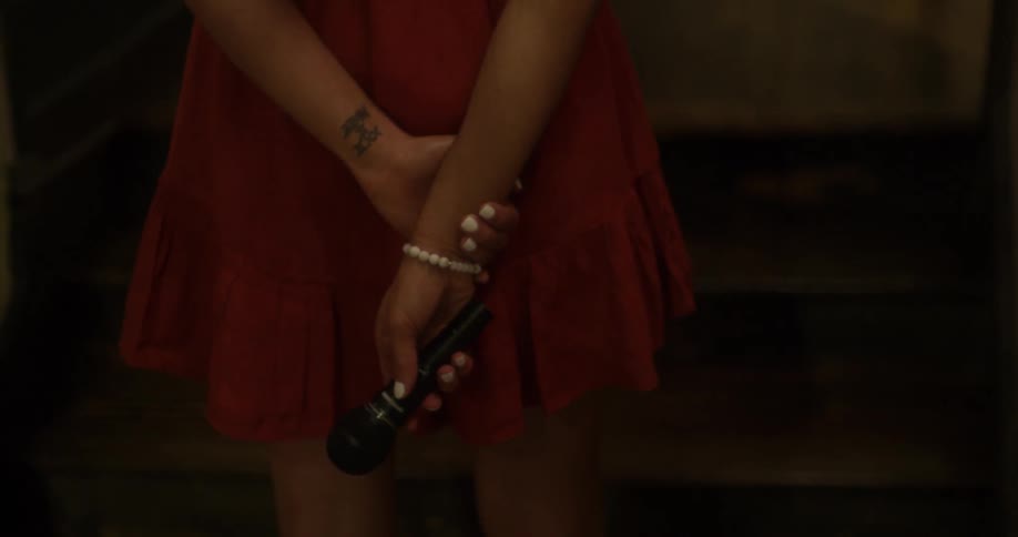 A woman holding a microphone fidgets her hands while she stands waiting