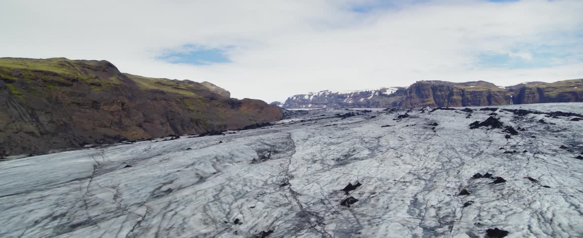 A rocky frozen landscape with rocky green hills in the background