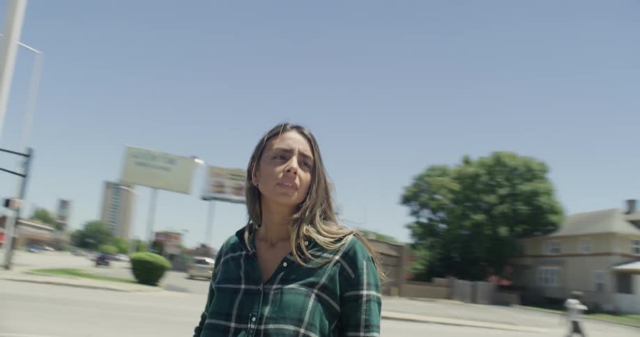 A woman takes a deep breath as she stands near a gas station on a sunny day