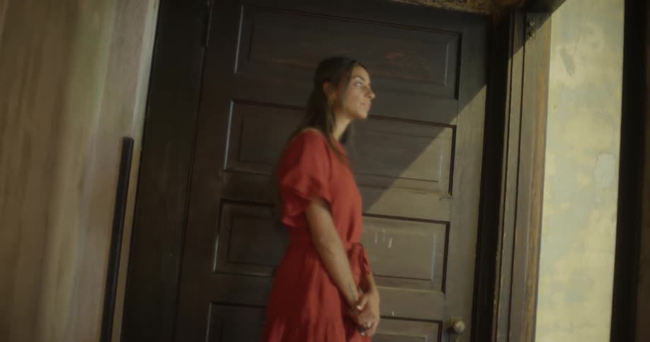 A woman holding a microphone walks up stairs and waits by a door