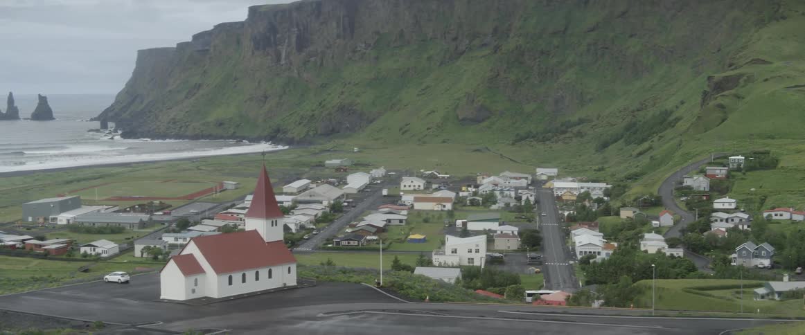 A town sits nestled at the base of cliffs near the ocean on a cloudy day