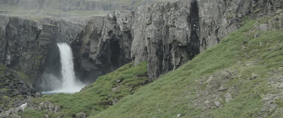A waterfall is cascading into a pool at the bottom of cliffs during the day