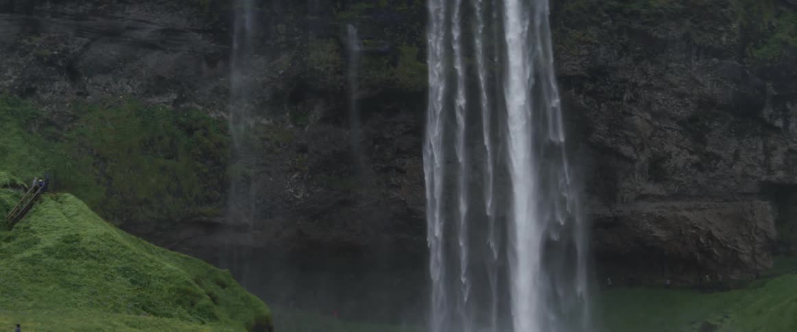 A waterfall is cascading into a pool at the bottom of cliffs during the day