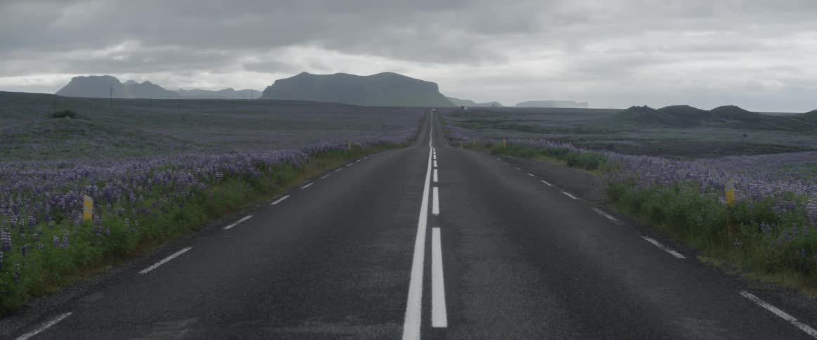 Storm clouds hang over a two-lane highway in a natural landscape