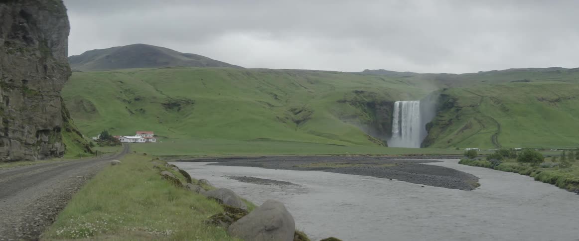 A building sits at the bottom of a green hill near a waterfall