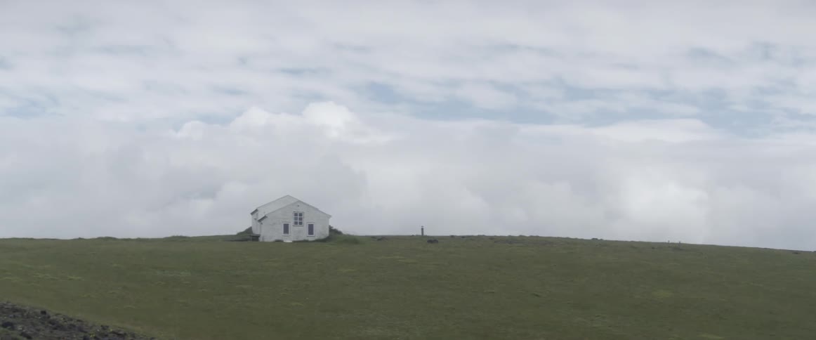 Clouds billow and hang over buildings on a rural hillside during the day