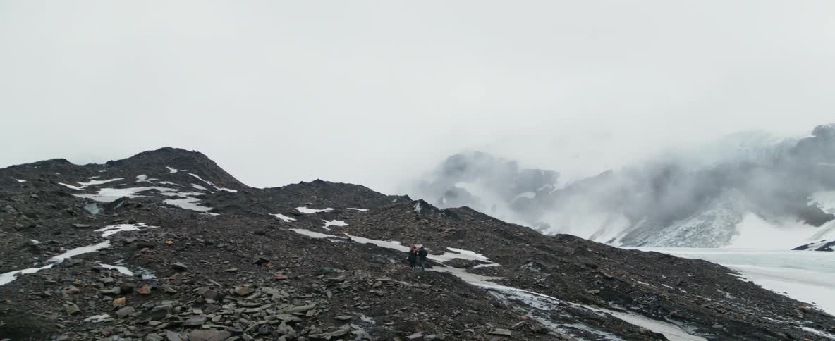Two people walking up a snowy rock covered hill