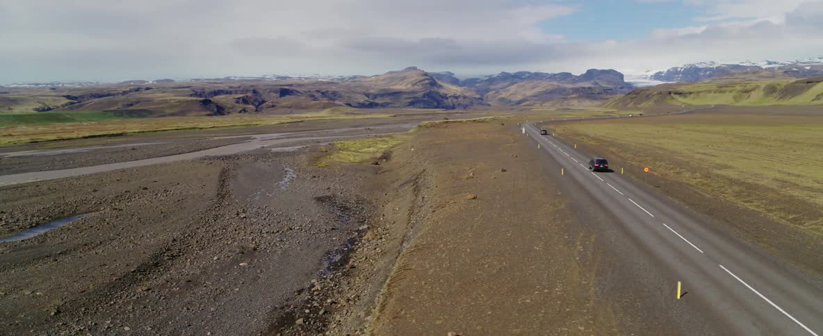 Vehicles drive on a two lane road in a mountain landscape during the day