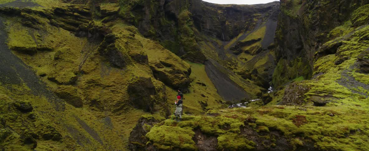 Two people stand at the edge of a cliff overlooking a river