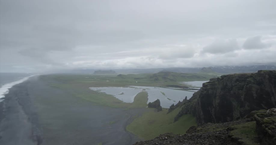 The shore has heavy clouds and many waves crashing