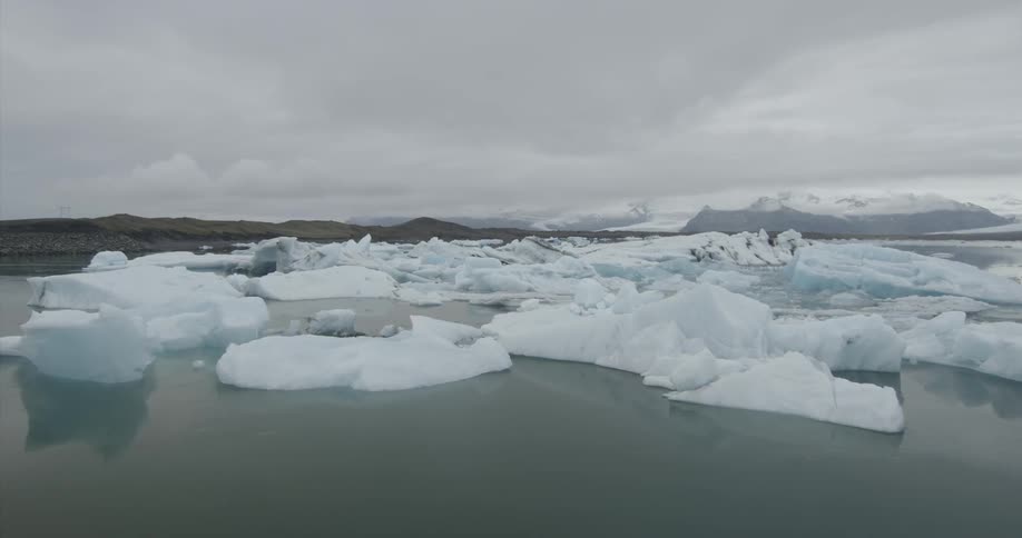 Ice and snow float in the ocean near shore on a cloudy day