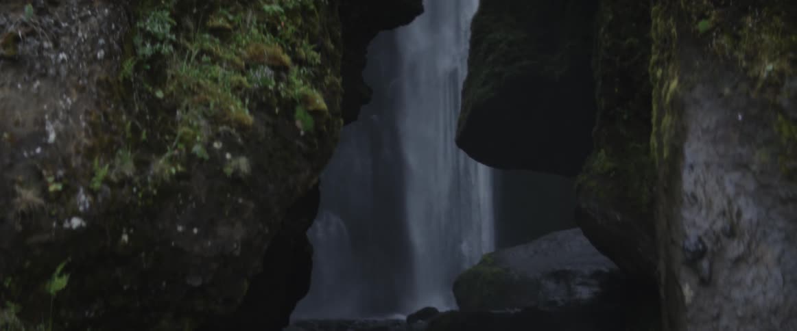 A waterfall is cascading into a pool and stream at the base of a ravine during the day