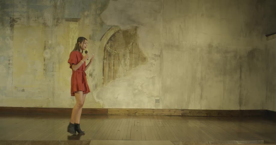 A woman in an orange dress paces on a stage