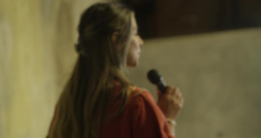 A woman carrying a microphone is walking onto a stage and raising her hand