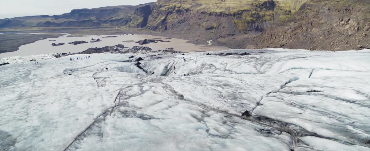A group of people is walking across a glacier during the day