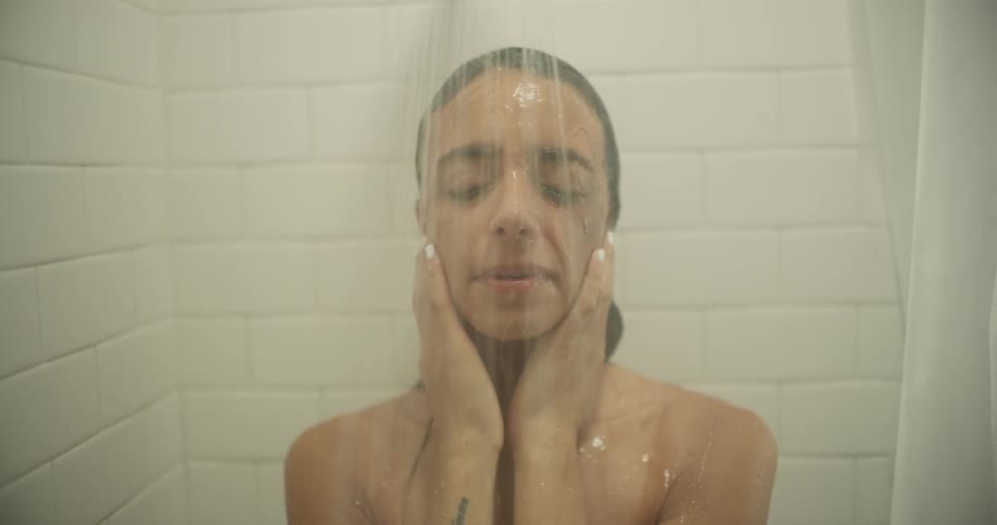 A woman is breathing deeply and holding her head as she takes a shower