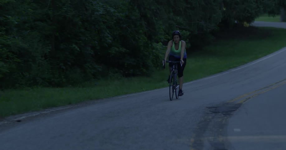 A woman rides a bicycle on a curving tree lined road