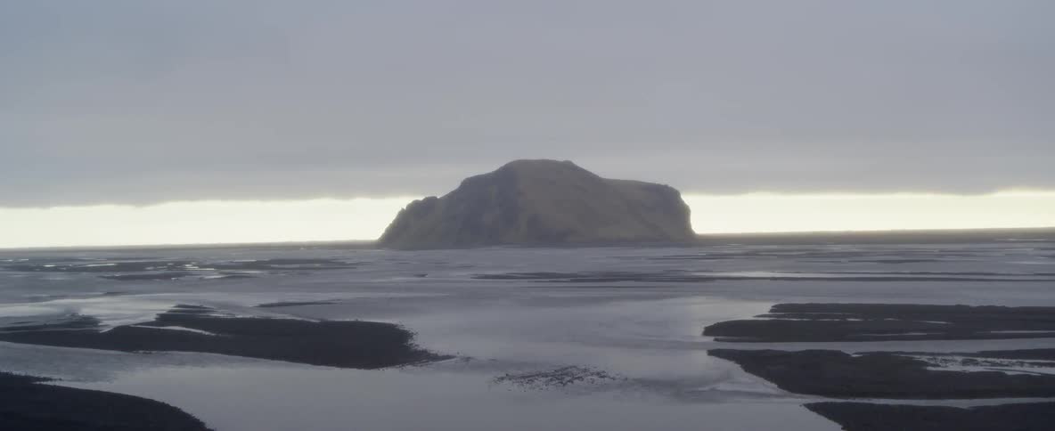 Storm clouds hover over a beach and island outcropping during the day