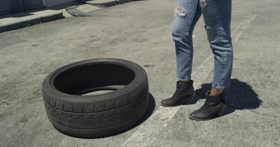 A woman stands by a tire in a gas station parking lot