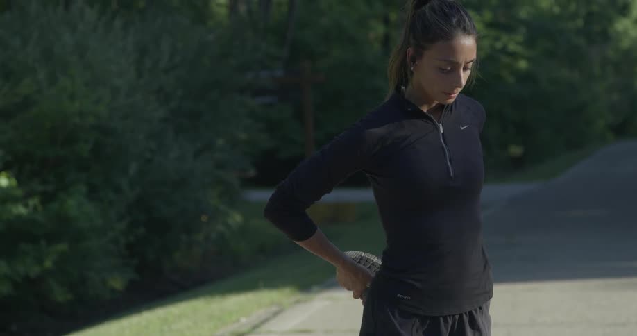 A woman is doing leg stretches on a road in the morning