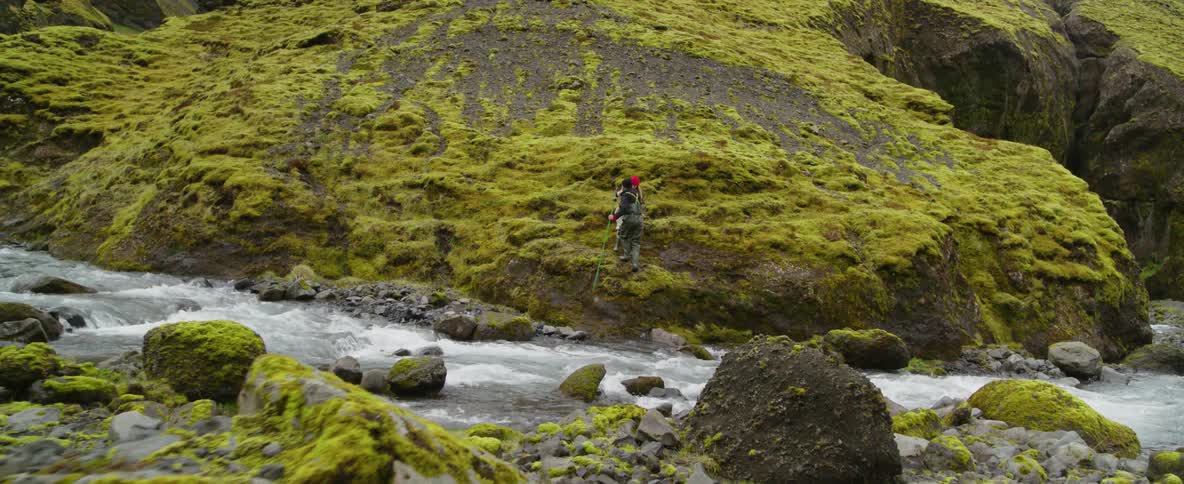Two people climb over a stream and up the mountain