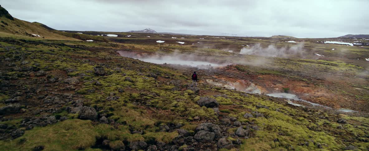 A person watches as steam rises from hot springs in a natural landscape during the day