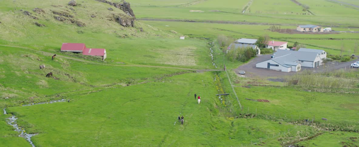 People ride horses across a rural field